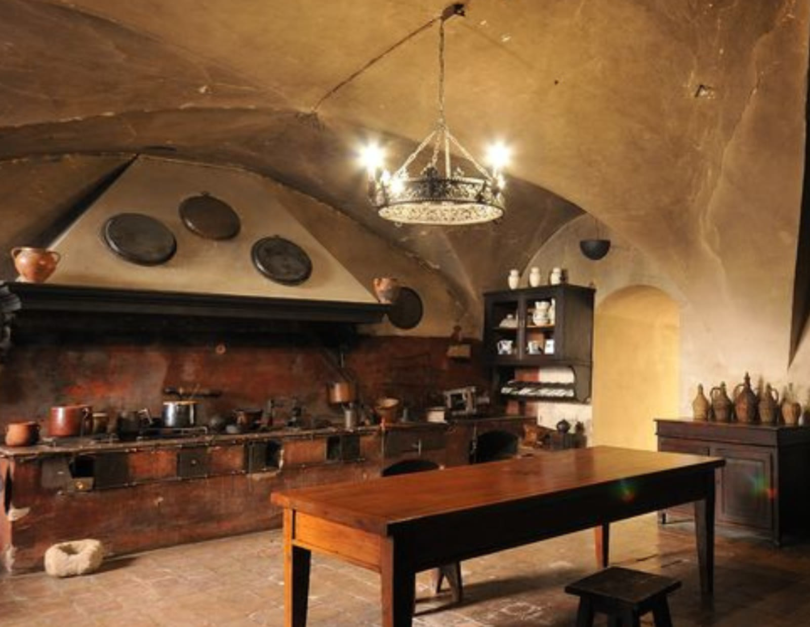 Masonry cooking range with copper pots and a wood table under a Tuscan vault