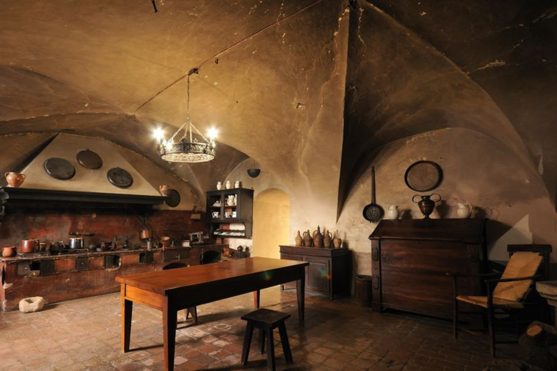 Vaulted Tuscan kitchen with a long wood table, masonry range and dark wood cabinet